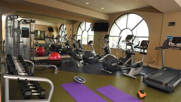 A gym with exercise equipment, mirrors, and large windows.