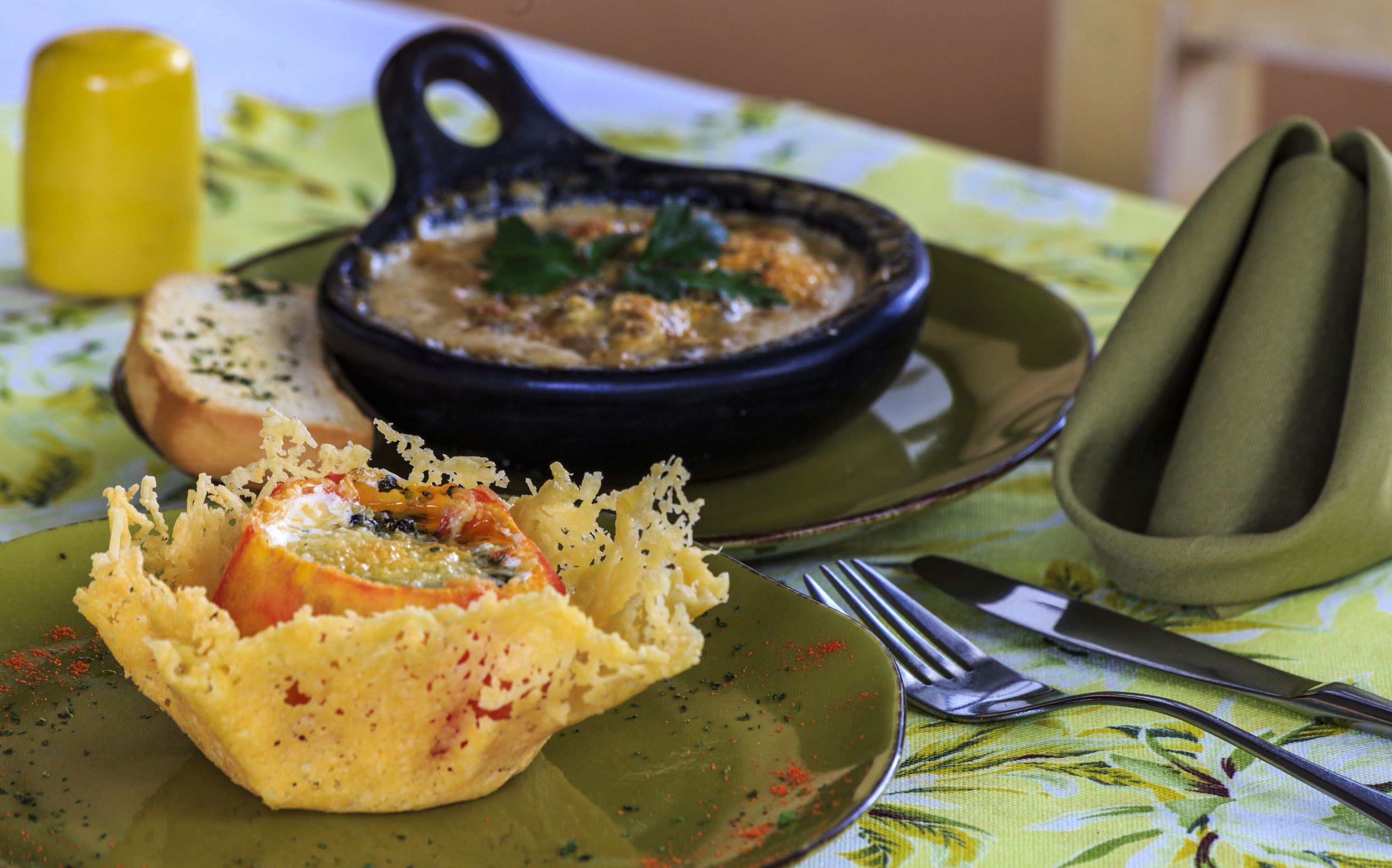 Una comida con un tazón de sopa y un plato al horno sobre una mesa con mantel de flores.