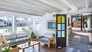 A room with a wooden bench, a sofa, and a table. There is a door with a colorful panel, and a window with a view of the outside. - Hotel & Spa Getsemaní (Villa de Leyva)