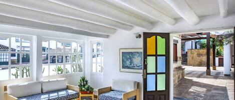 Una habitación con un banco de madera, un sofá y una mesa. Hay una puerta con un panel colorido y una ventana que da al exterior.