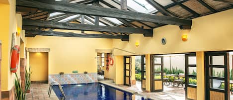An indoor swimming pool with a vaulted ceiling, tiled walls, and a view of the outdoors.
