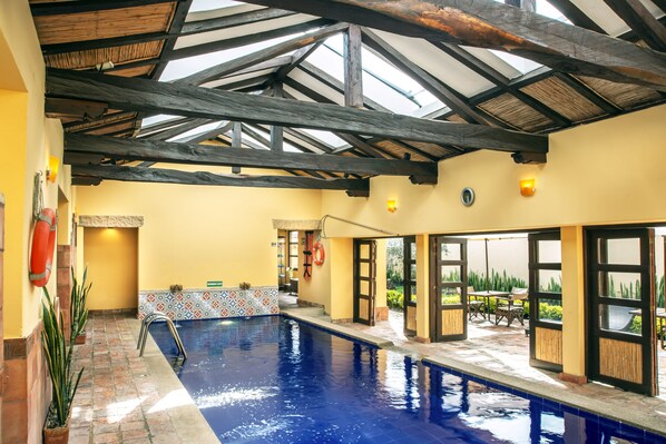 Una piscina interior con techo abovedado, paredes enlosadas y vistas al exterior.
