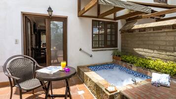 A patio with a hot tub, a table with a chair, and a door leading to an interior space.