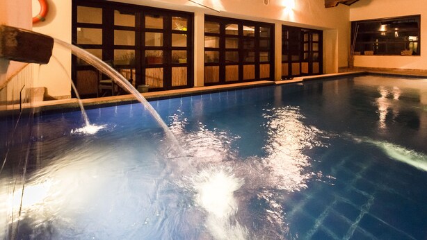 An indoor swimming pool with clear water, a water feature, and a view of the outside through large windows. - Hotel & Spa Getsemaní (Villa de Leyva)