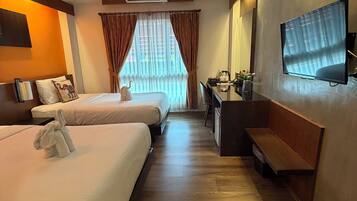 Ein Hotelzimmer mit zwei Betten, einem Schreibtisch, einem Fernseher und einem Fenster mit Vorhängen.