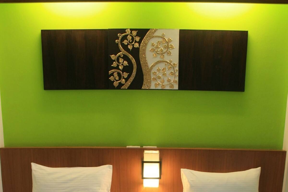 A hotel room with two beds, a wooden headboard, a wall-mounted light, and a green wall.