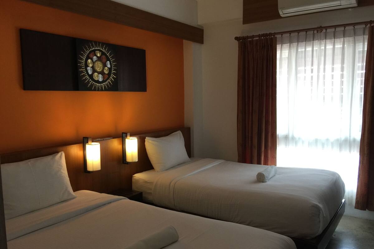 A hotel room with two beds, a wall-mounted artwork, and a window with curtains.