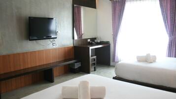 A hotel room with a flat-screen TV, a desk with a mirror, a bed with white linens, and a window with purple curtains.