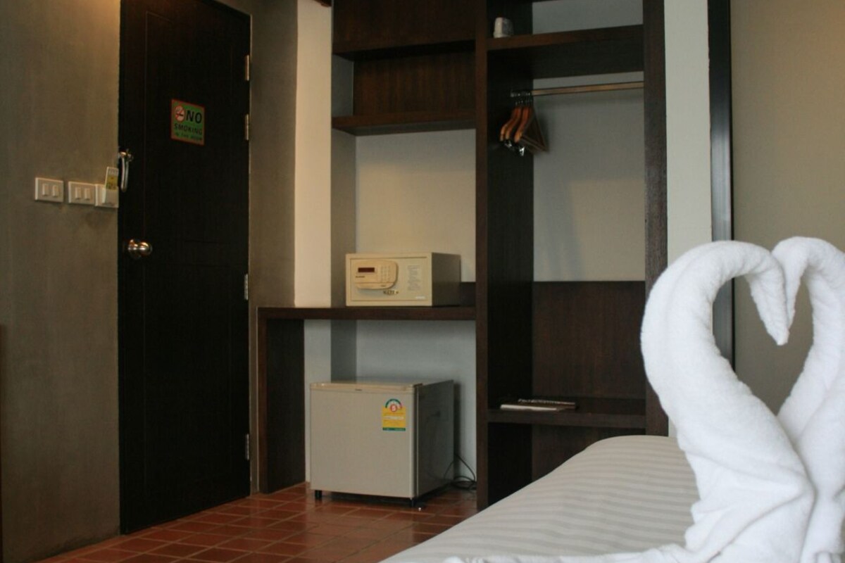 Habitación de hotel con cama, minibar, perchero y puerta con letrero de 'No Fumar'.