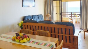 A dining area with a wooden table, chairs, and a fruit basket. There is a balcony with a view of the sea. - First Group Costa Smeralda (Margate)