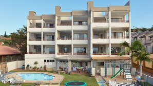 A multi-story hotel with a swimming pool, outdoor seating, and a children's play area. - First Group Costa Smeralda (Margate)