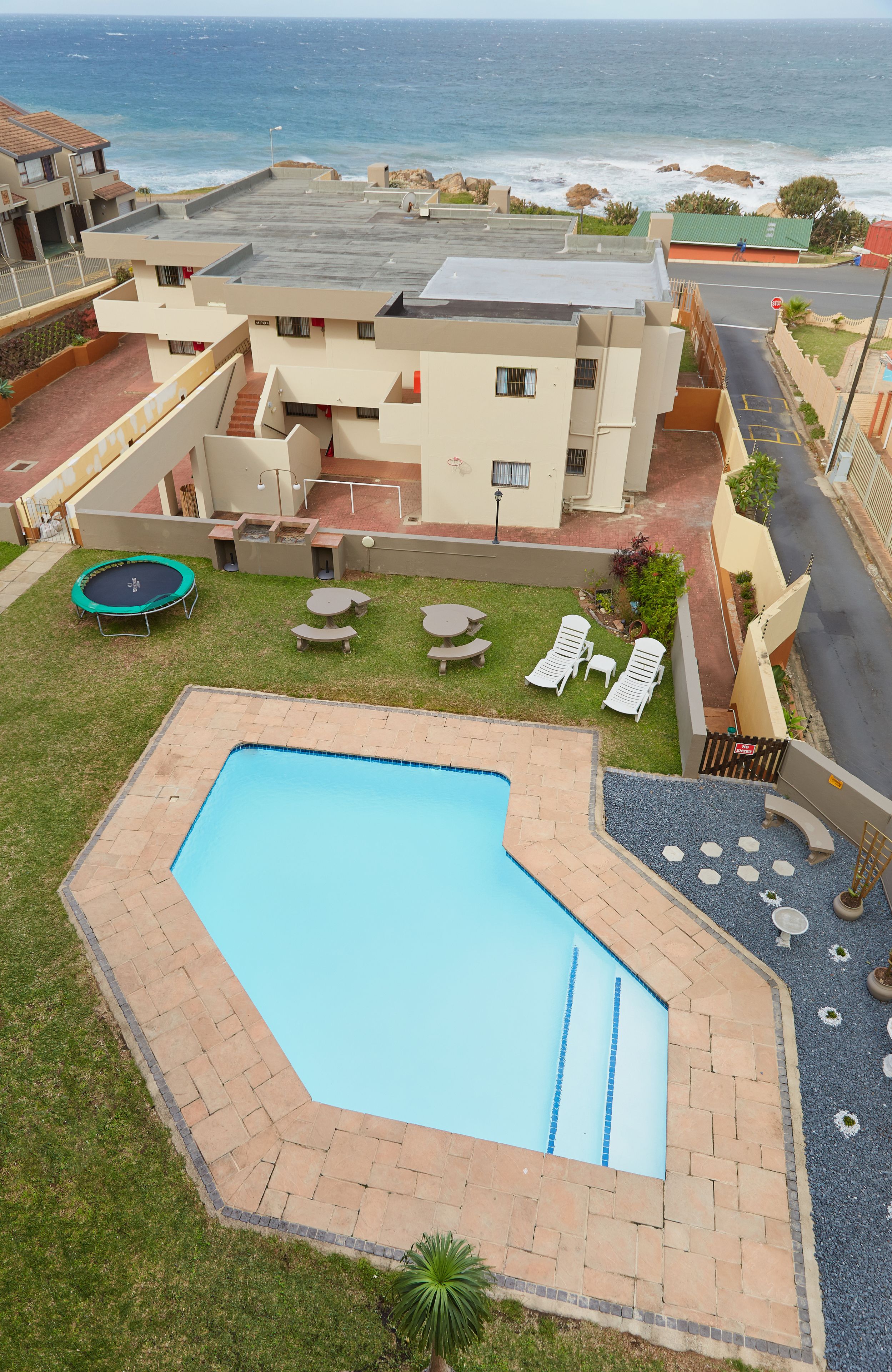 A swimming pool with a view of the ocean, a trampoline, and outdoor seating.