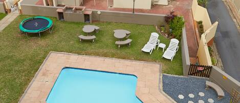A swimming pool with a view of the ocean, a trampoline, and outdoor seating.
