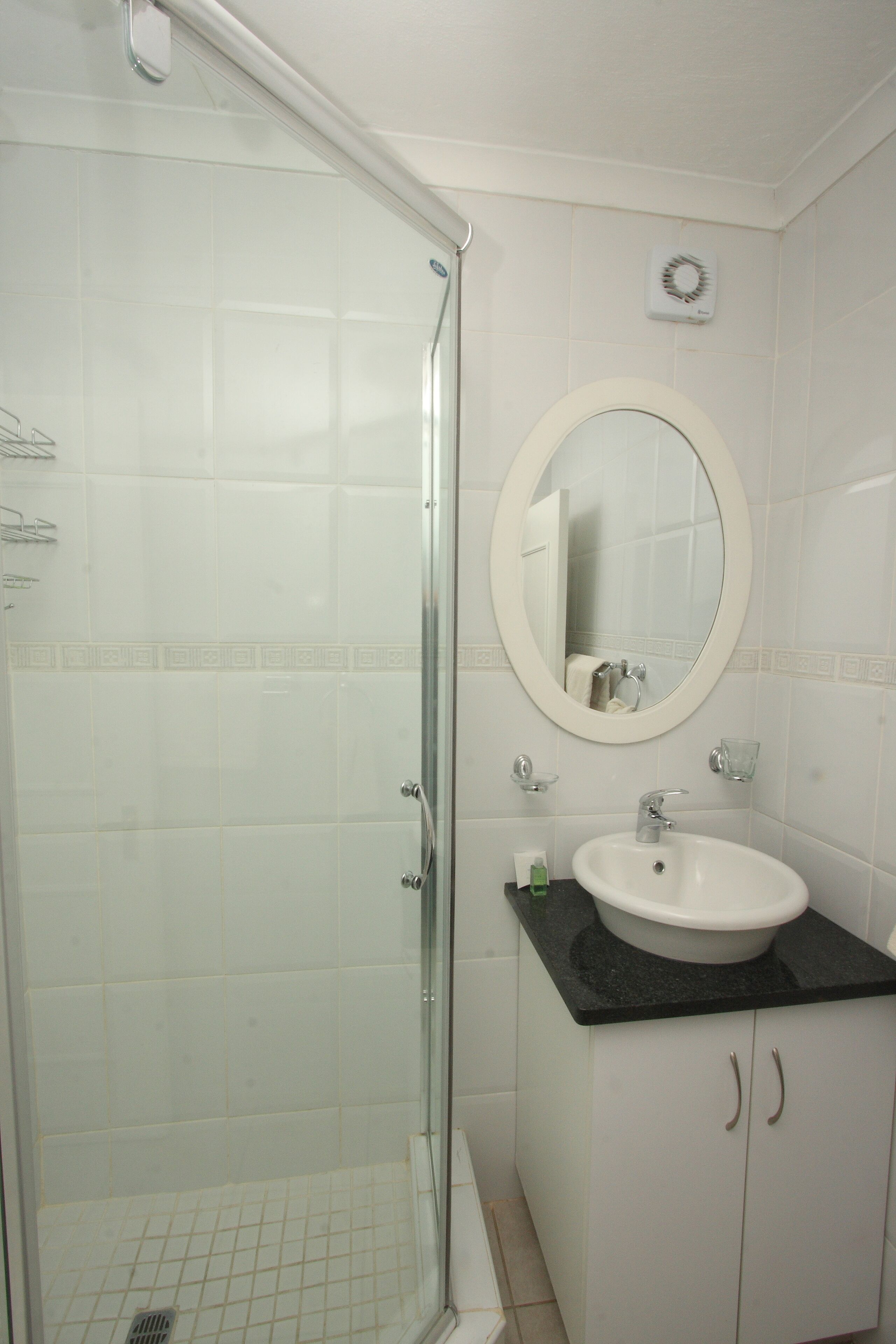Casa de banho com cabine de duche em vidro, lavatório branco com bancada preta e espelho redondo sobre o lavatório.