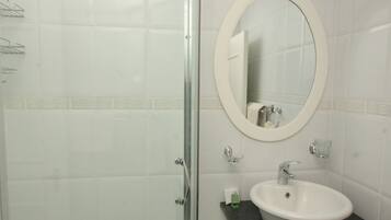 A bathroom with a glass shower enclosure, a white sink with a black countertop, and a round mirror above the sink.