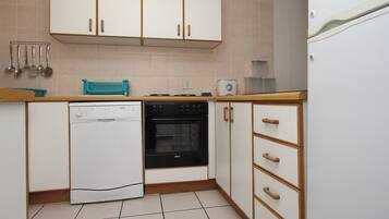Una cocina compacta con gabinetes blancos, lavavajillas, horno y refrigerador.