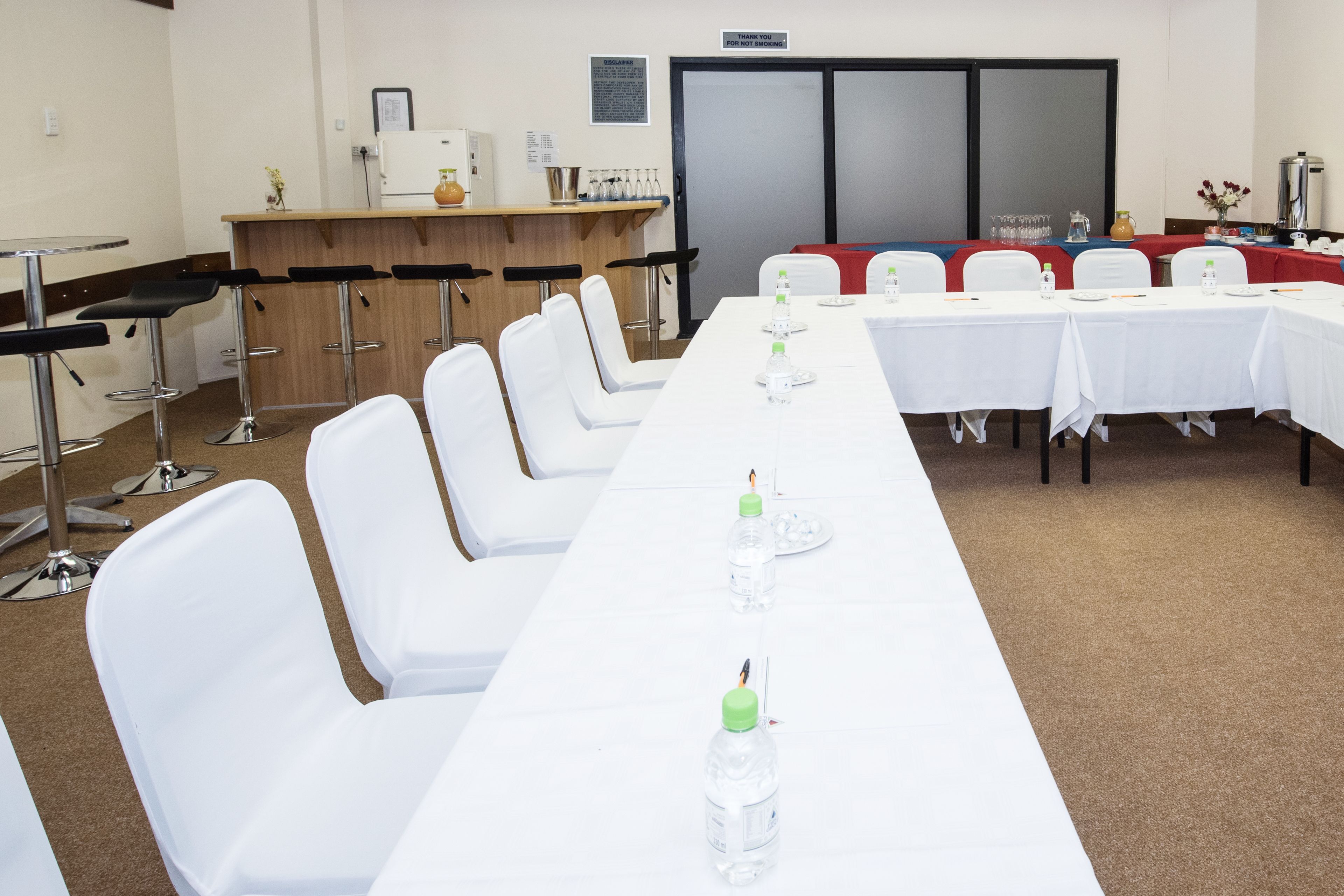 Un salón de conferencias con una larga mesa, sillas blancas y una zona de bar con taburetes.