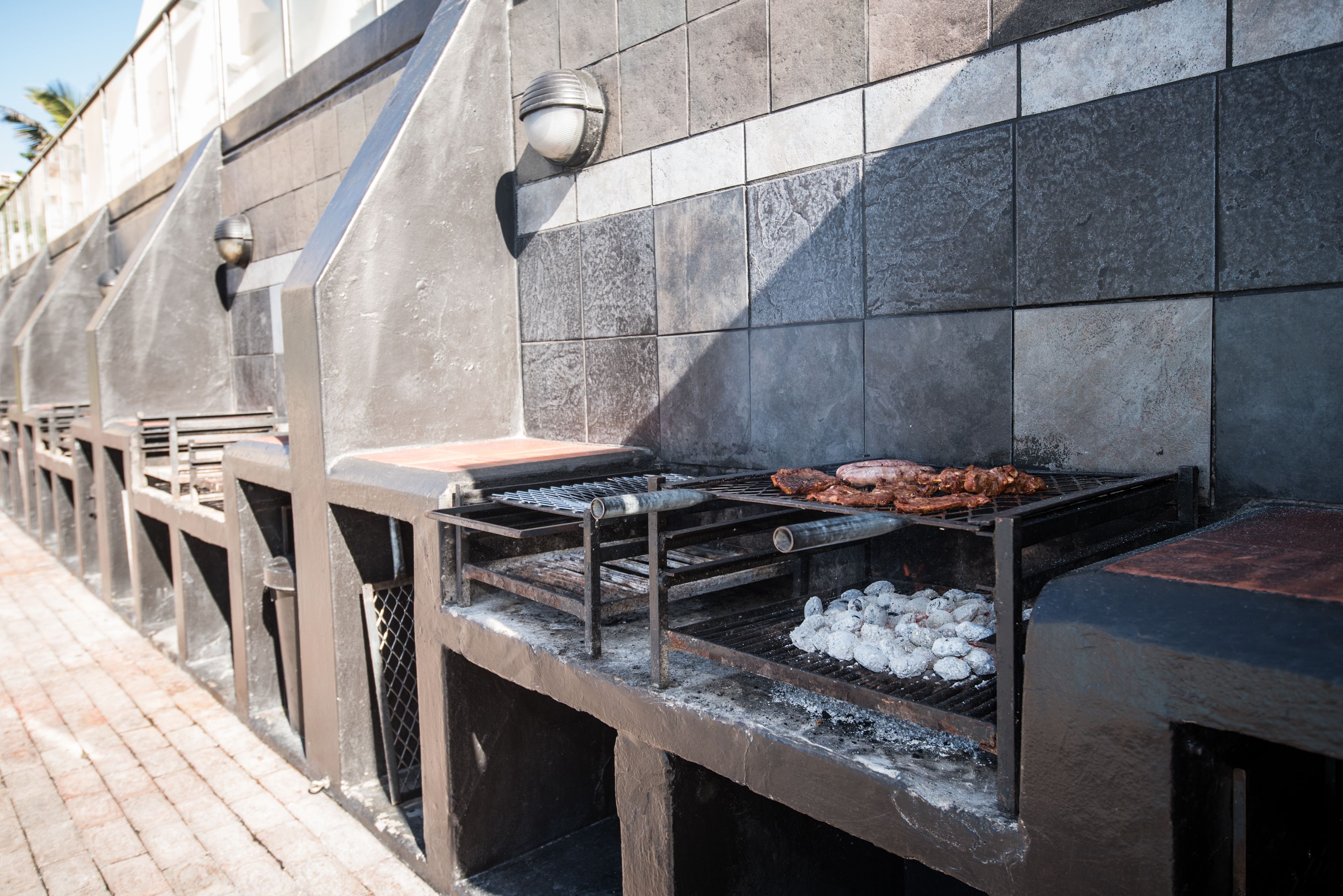 A barbecue grill with meat and charcoal, set against a tiled wall.