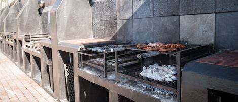 A barbecue grill with meat and charcoal, set against a tiled wall.