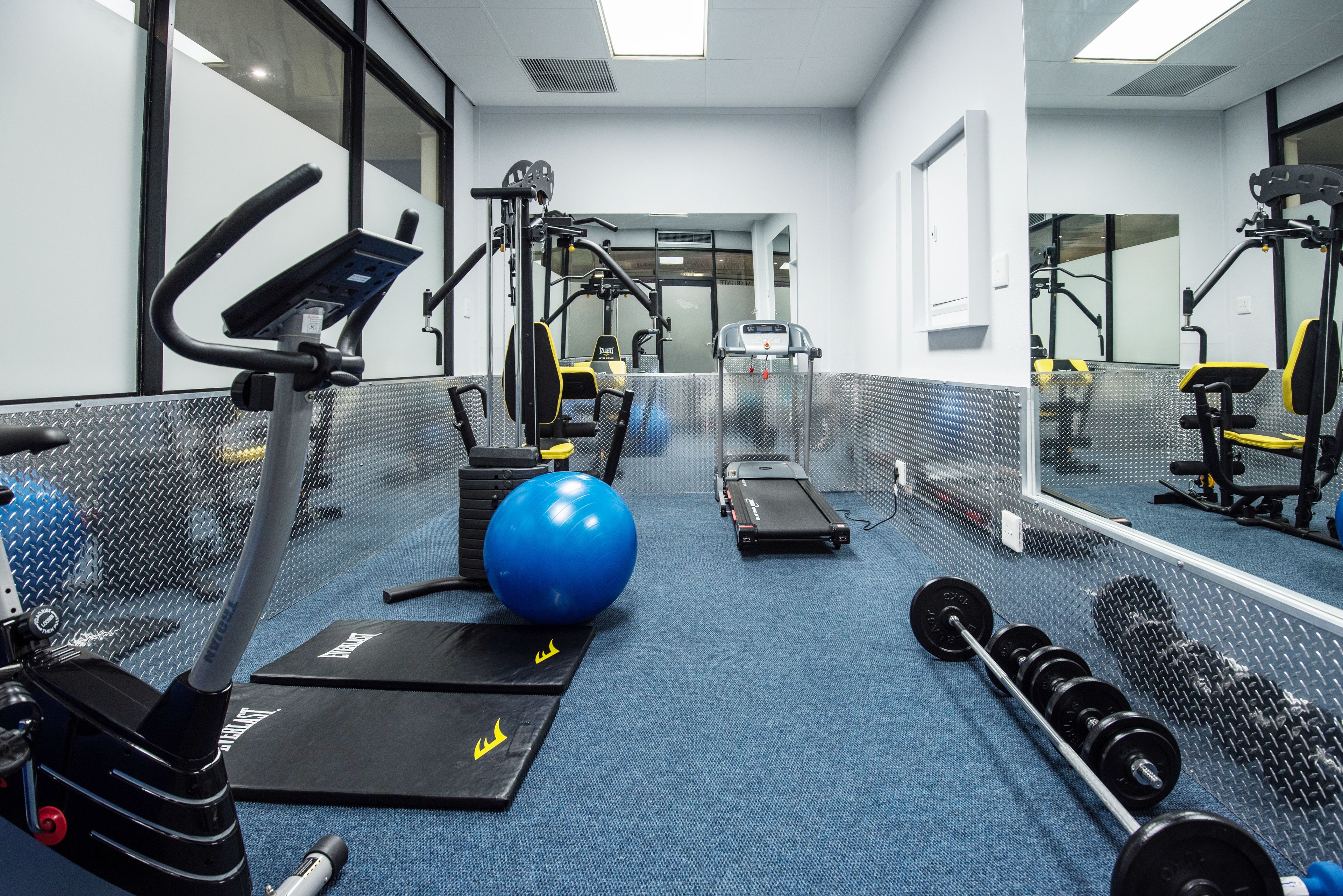 A gym with exercise equipment, a blue exercise ball, and a treadmill.
