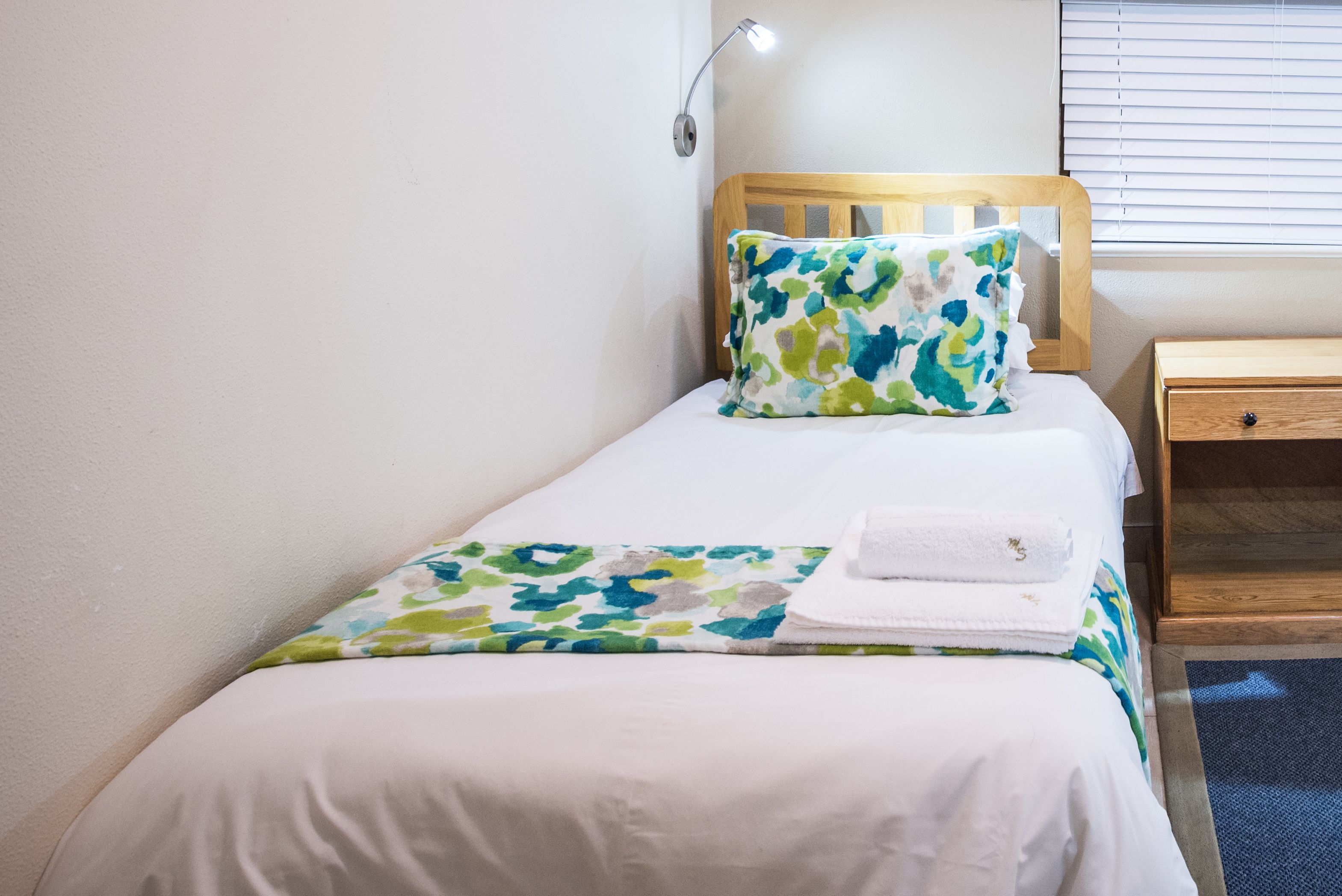 A neatly made bed with a floral pillow and a folded towel on a white bedspread.