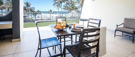A dining area with a table set for four, a view of the beach, and a balcony with a railing.