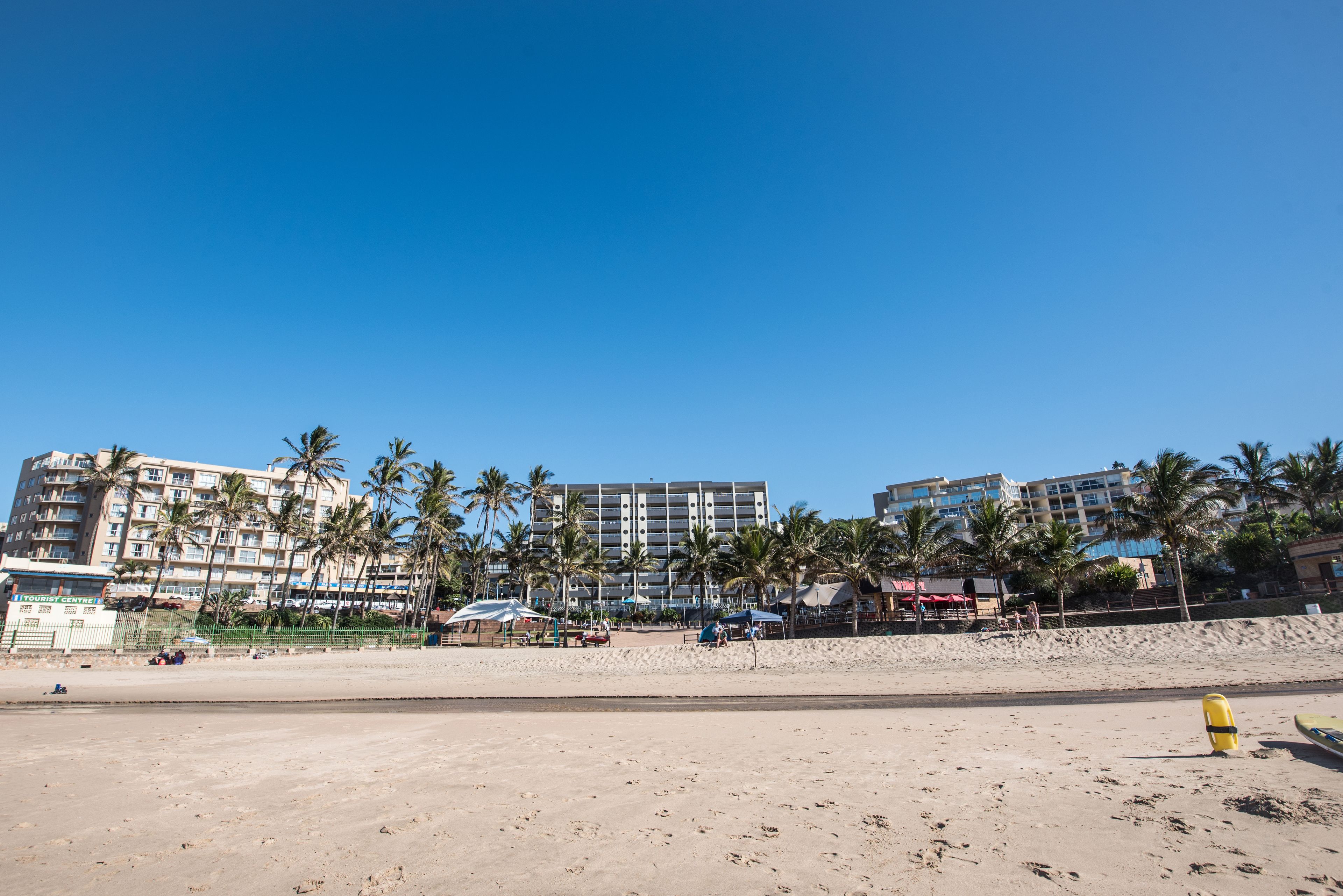 Een strand met een zandstrand, palmbomen en een hotel op de achtergrond.