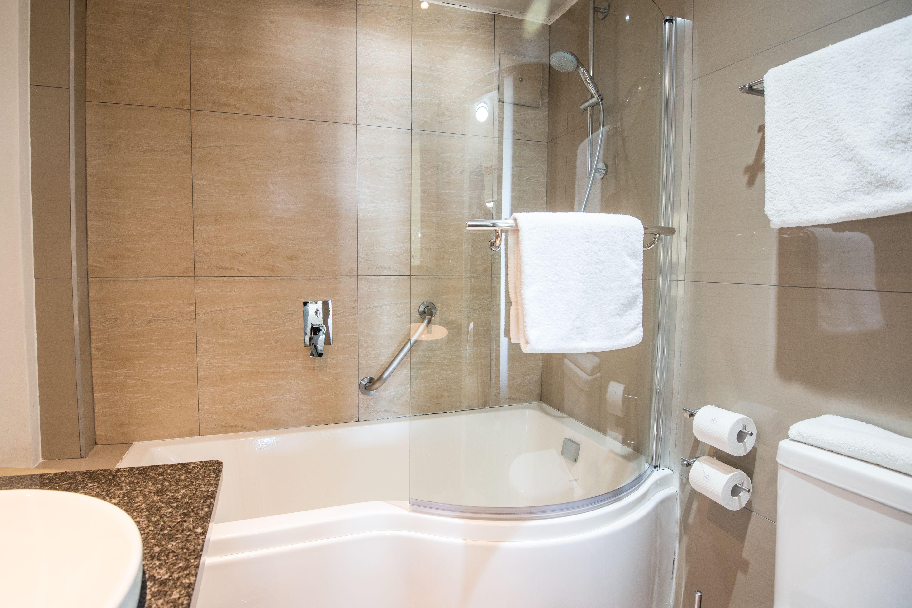Et stilfuldt badeværelse med en glasafskærmet brusekabine, et hvidt badekar og et toilet.