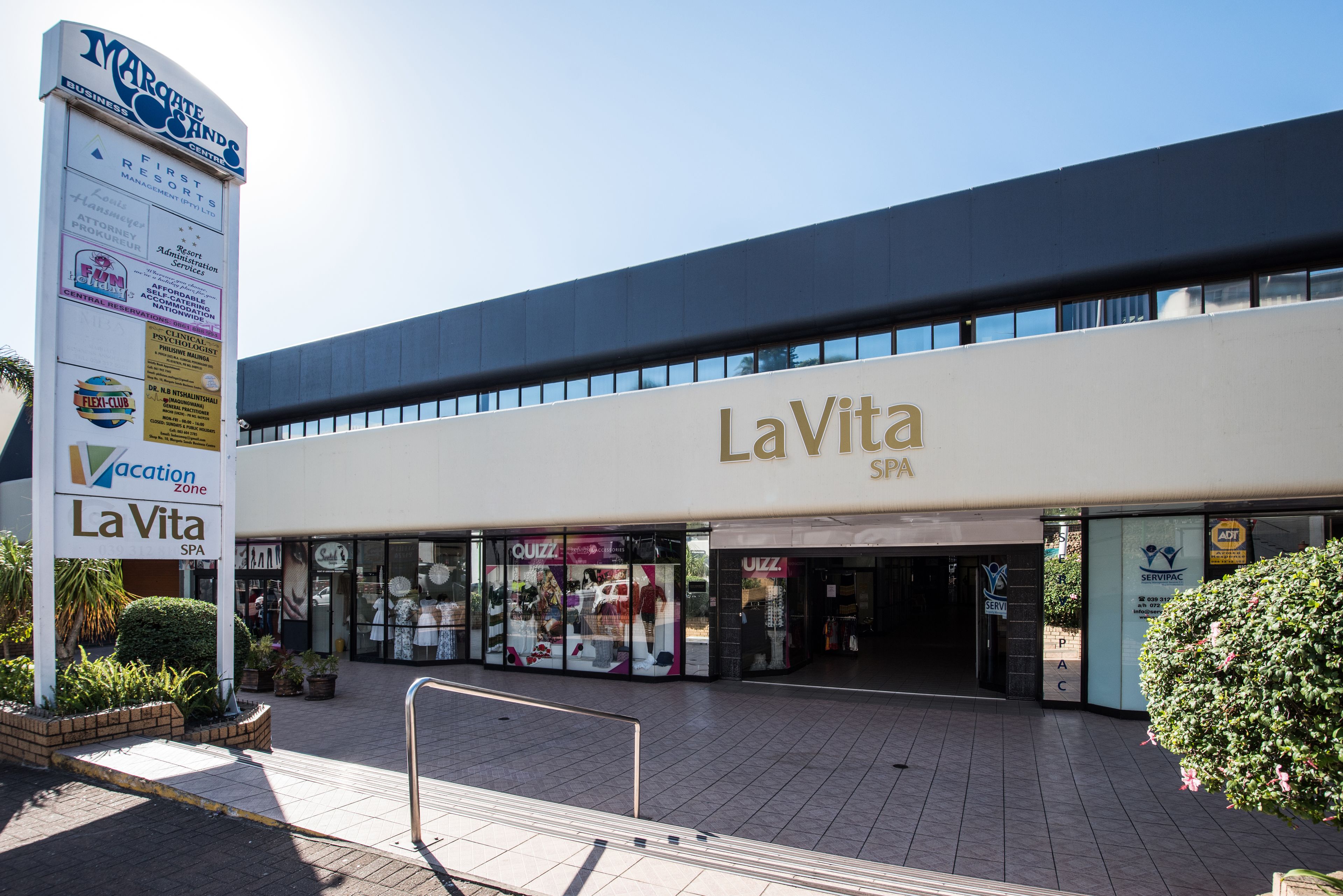 A La Vita SPA building with a large sign, storefronts, and a clear sky.