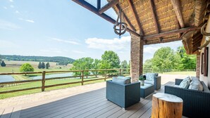 A covered outdoor area with wicker furniture and a view of a lake and fields. - Whispering Waters (Nottingham Road)