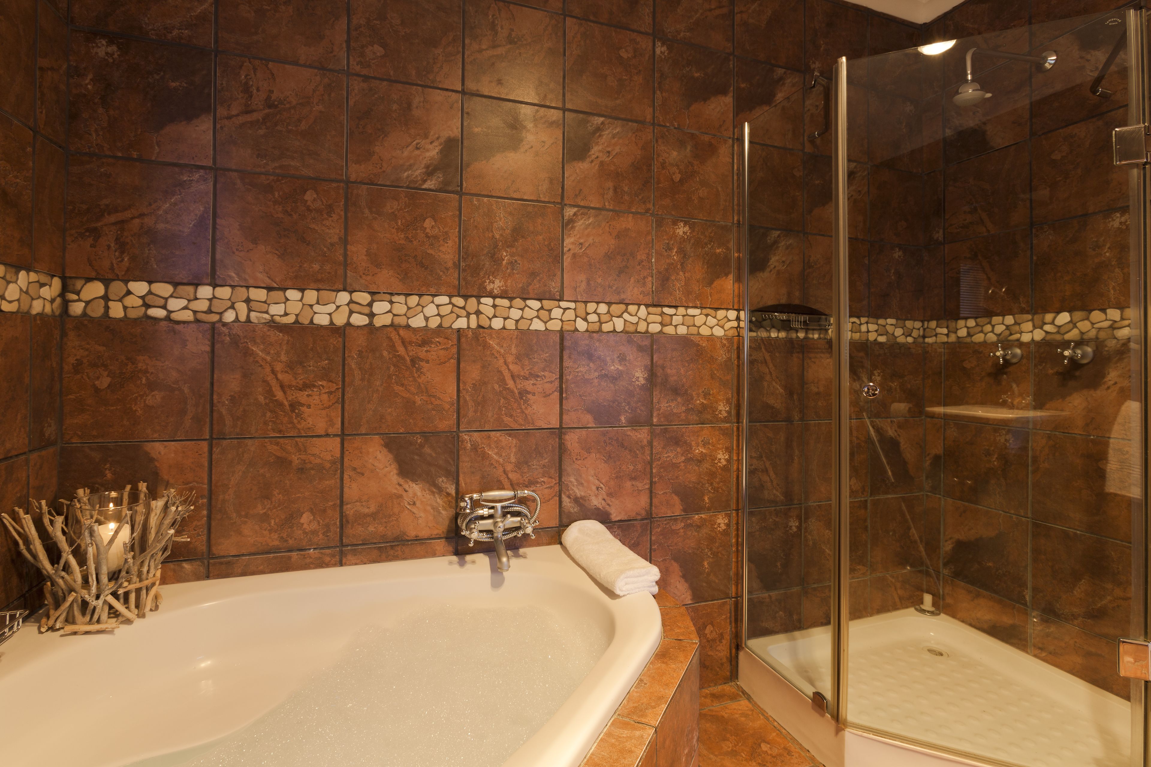 A bathroom with a bathtub, a glass-enclosed shower, and a stone mosaic border.