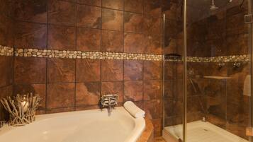 A bathroom with a bathtub, a glass-enclosed shower, and a stone mosaic border.
