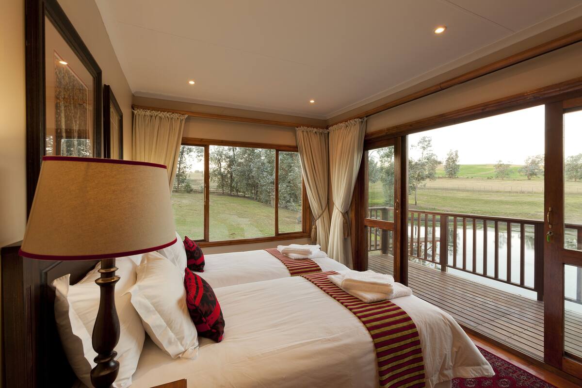 Une chambre avec deux lits, une grande fenêtre avec des rideaux et une vue sur un paysage verdoyant.