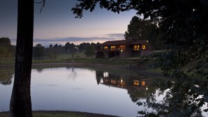 A lakeside building with a reflection in the water, surrounded by trees and a fence. - Whispering Waters (Nottingham Road)