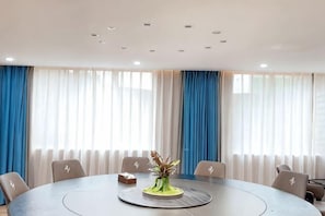 Una sala de conferencias con una mesa redonda, sillas, un florero con flores y cortinas.