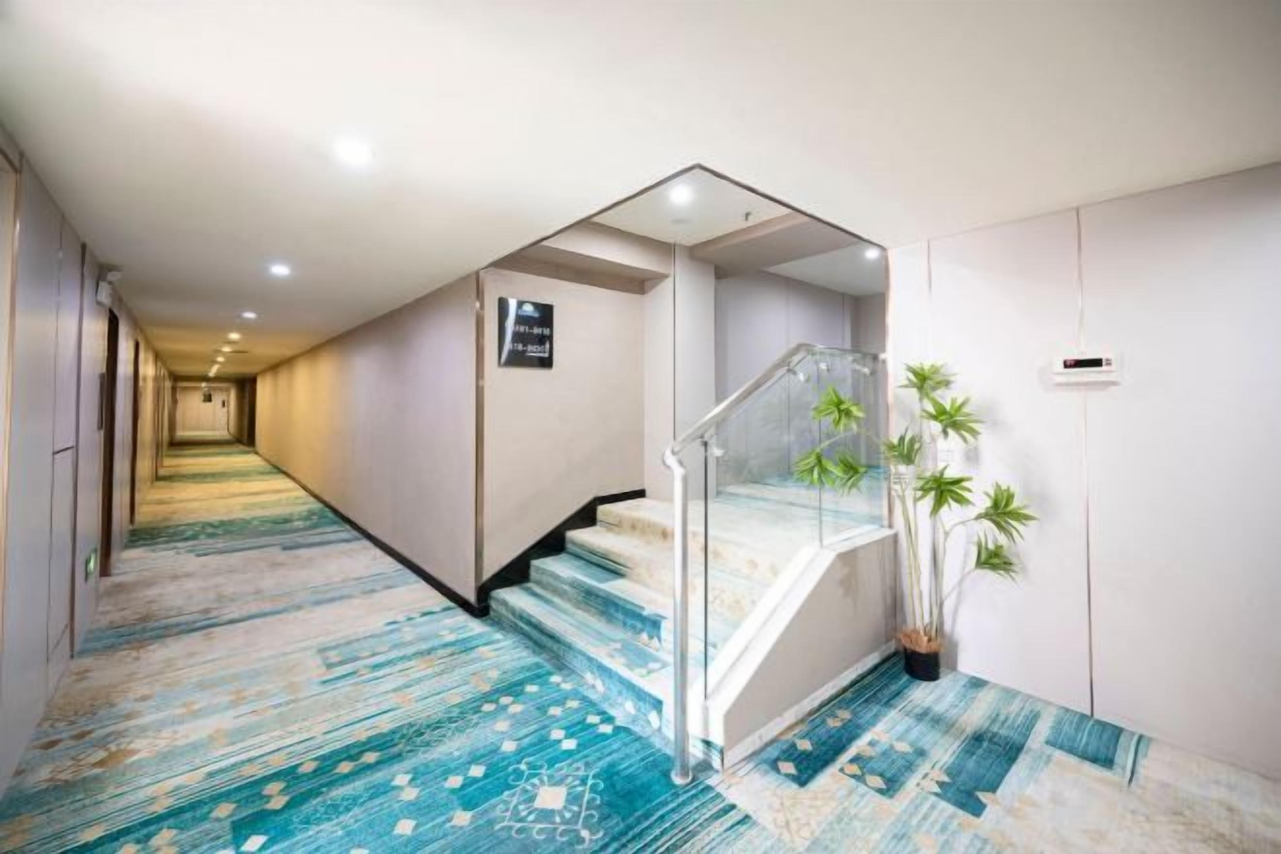 Un couloir d’hôtel avec un escalier recouvert de moquette, une plante et un panneau sur le mur.