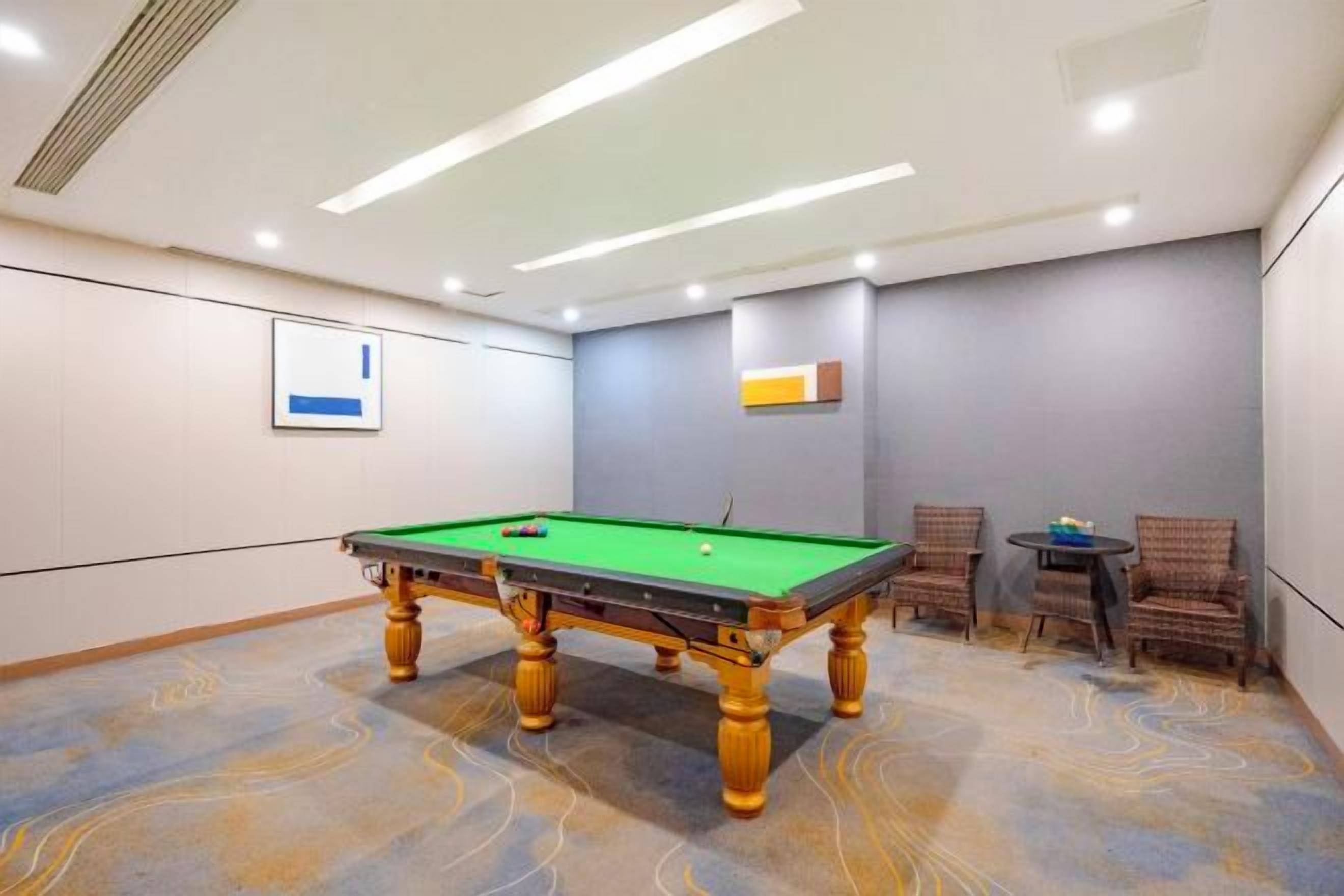A pool table in a room with a patterned carpet, two chairs, and a small table.