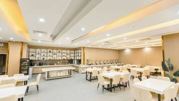 A spacious dining area with multiple tables and chairs, a central counter, and a kitchen in the background.