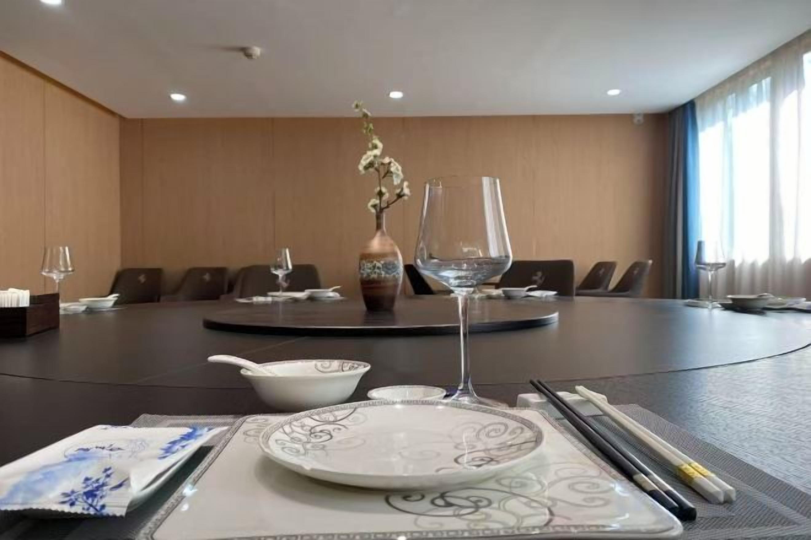 Une salle de conférence avec une table ronde, des chaises, un vase rempli de fleurs et un verre posé sur la table.