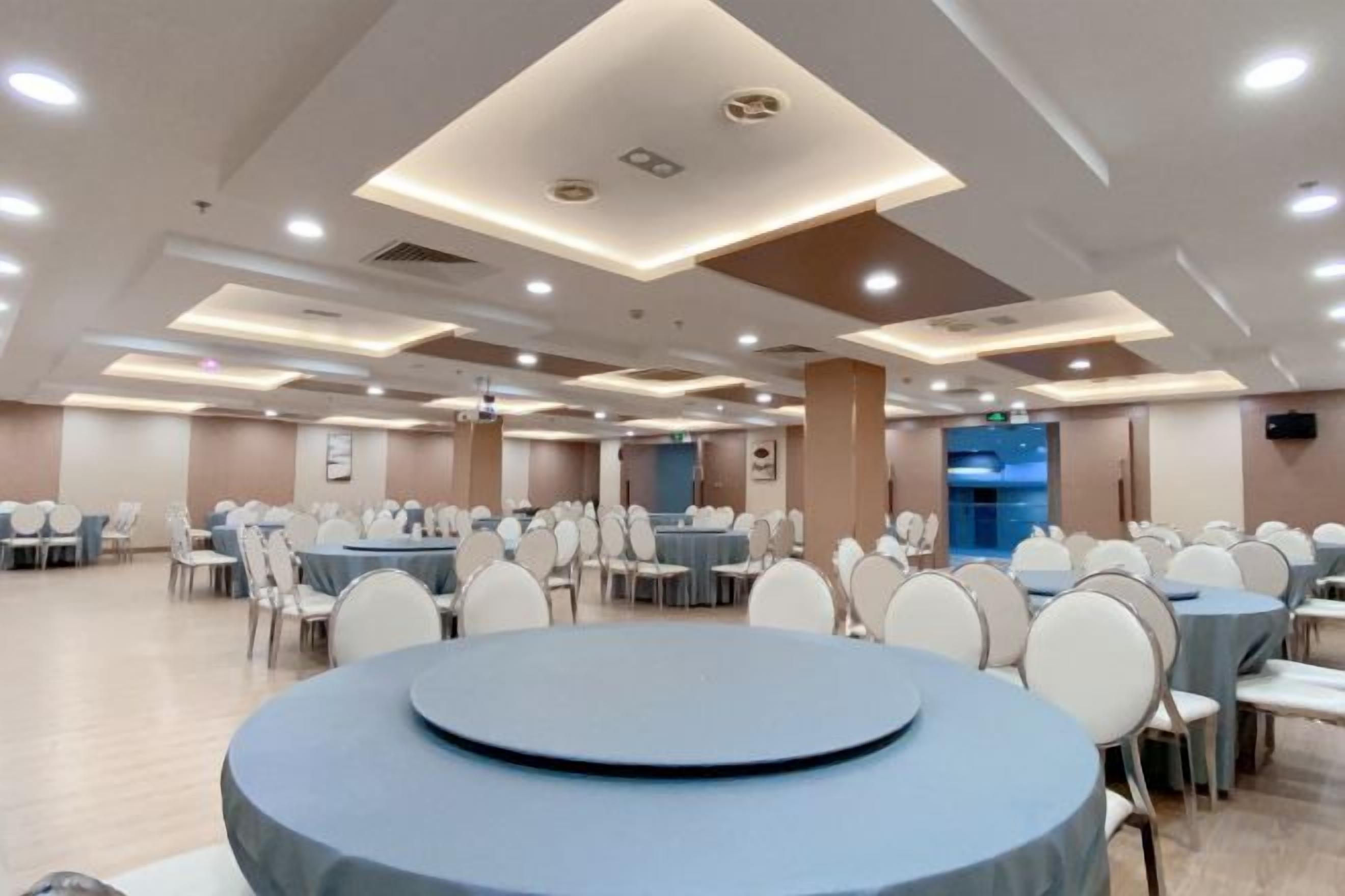 A banquet hall with round tables and chairs, recessed lighting, and a blue accent wall.