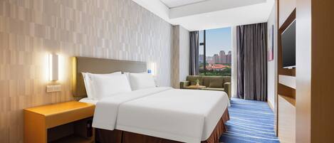 Een hotelkamer met een groot bed, een nachtkastje, een televisie en uitzicht op een stadsgezicht.