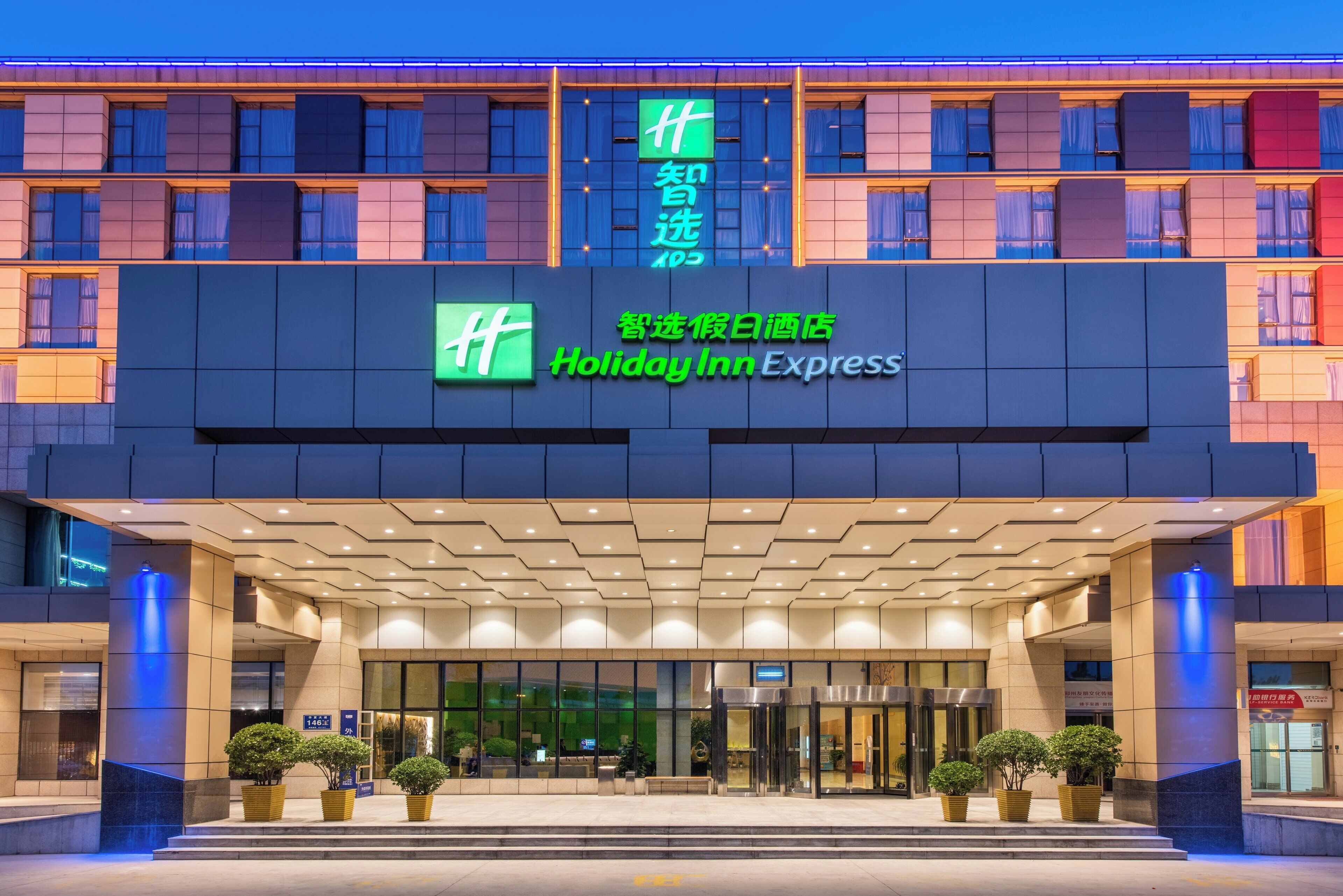 A Holiday Inn Express hotel entrance with a modern facade, large windows, and a welcoming entrance area with potted plants.