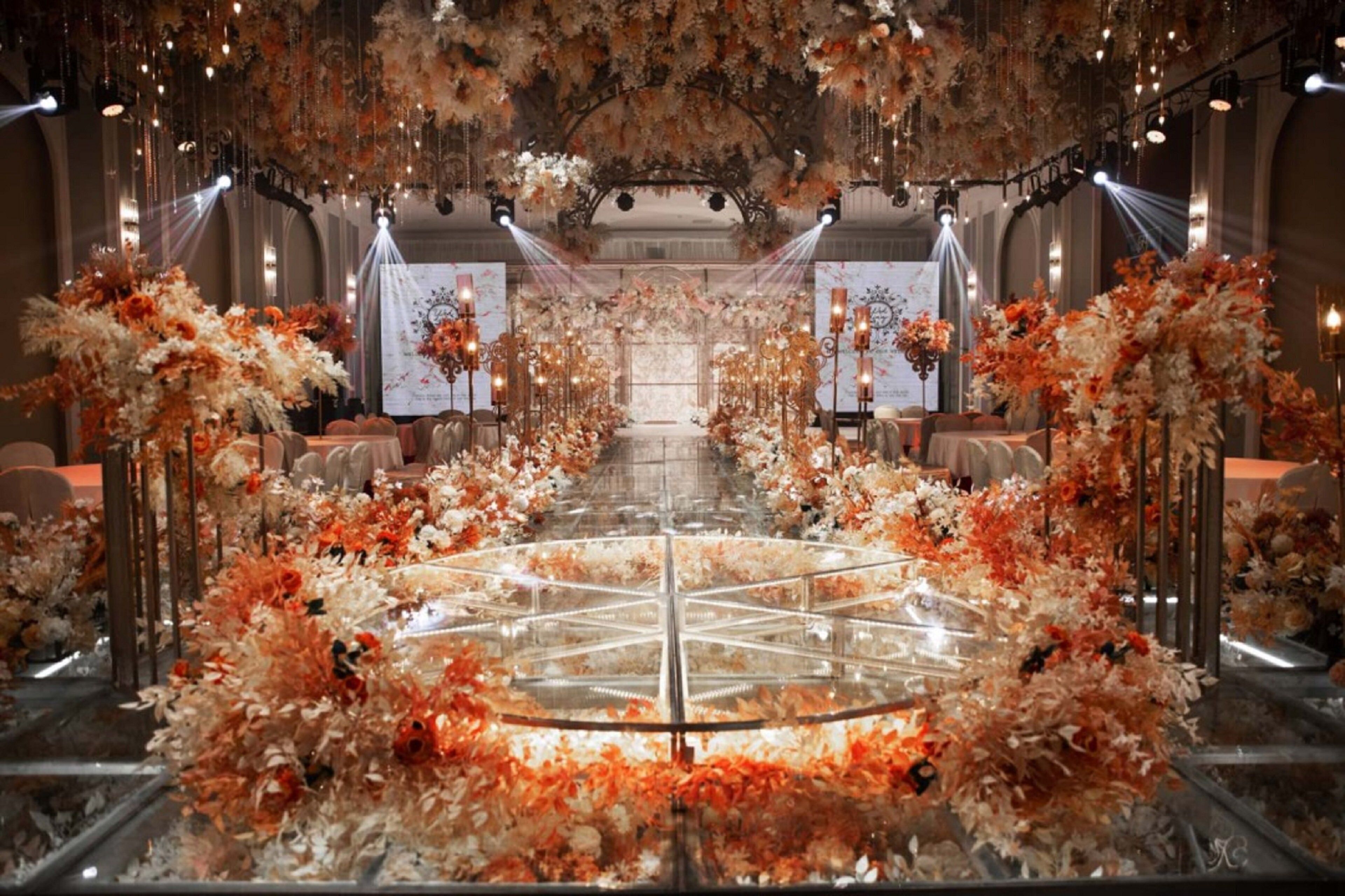 A grand hall with a central circular platform surrounded by floral arrangements and tables.