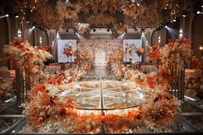 A grand hall with a central circular platform surrounded by floral arrangements and tables.