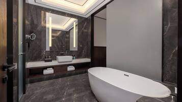 Un baño moderno con una bañera independiente, suelo de mármol oscuro y un espejo grande sobre el lavabo.