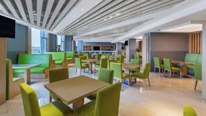 Un espace de repas moderne avec des sièges et des tables de couleur verte, une cuisine en arrière-plan et un plafond doté de luminaires linéaires.