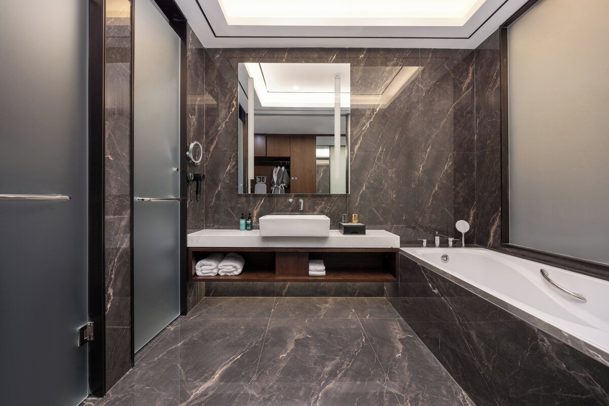 Une salle de bain moderne avec un grand miroir, une baignoire et un meuble-lavabo doté d’un évier et d’un porte-serviettes.