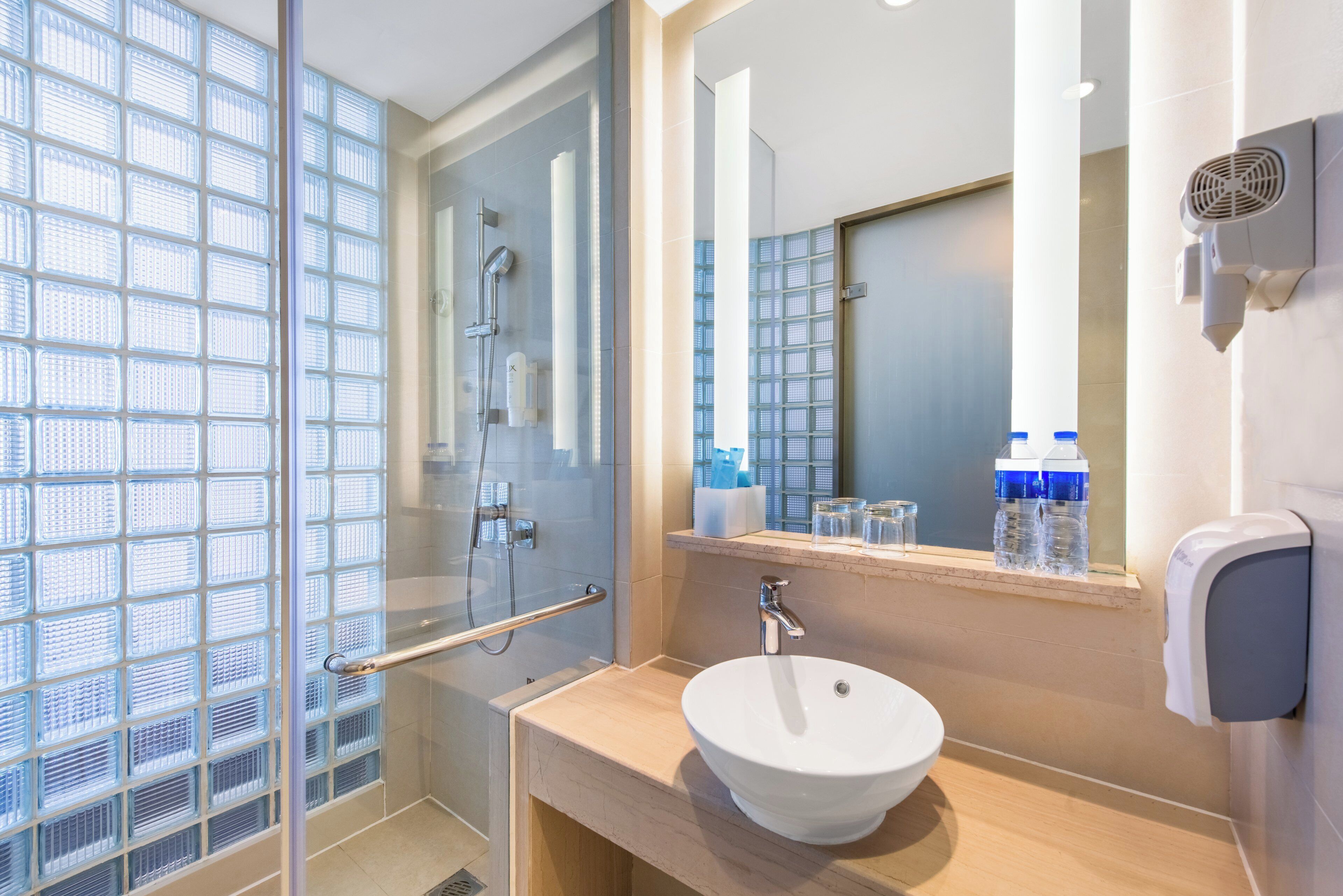 Une salle de bain moderne avec une douche à parois de verre, un lavabo blanc et un miroir doté d’un sèche-mains intégré.