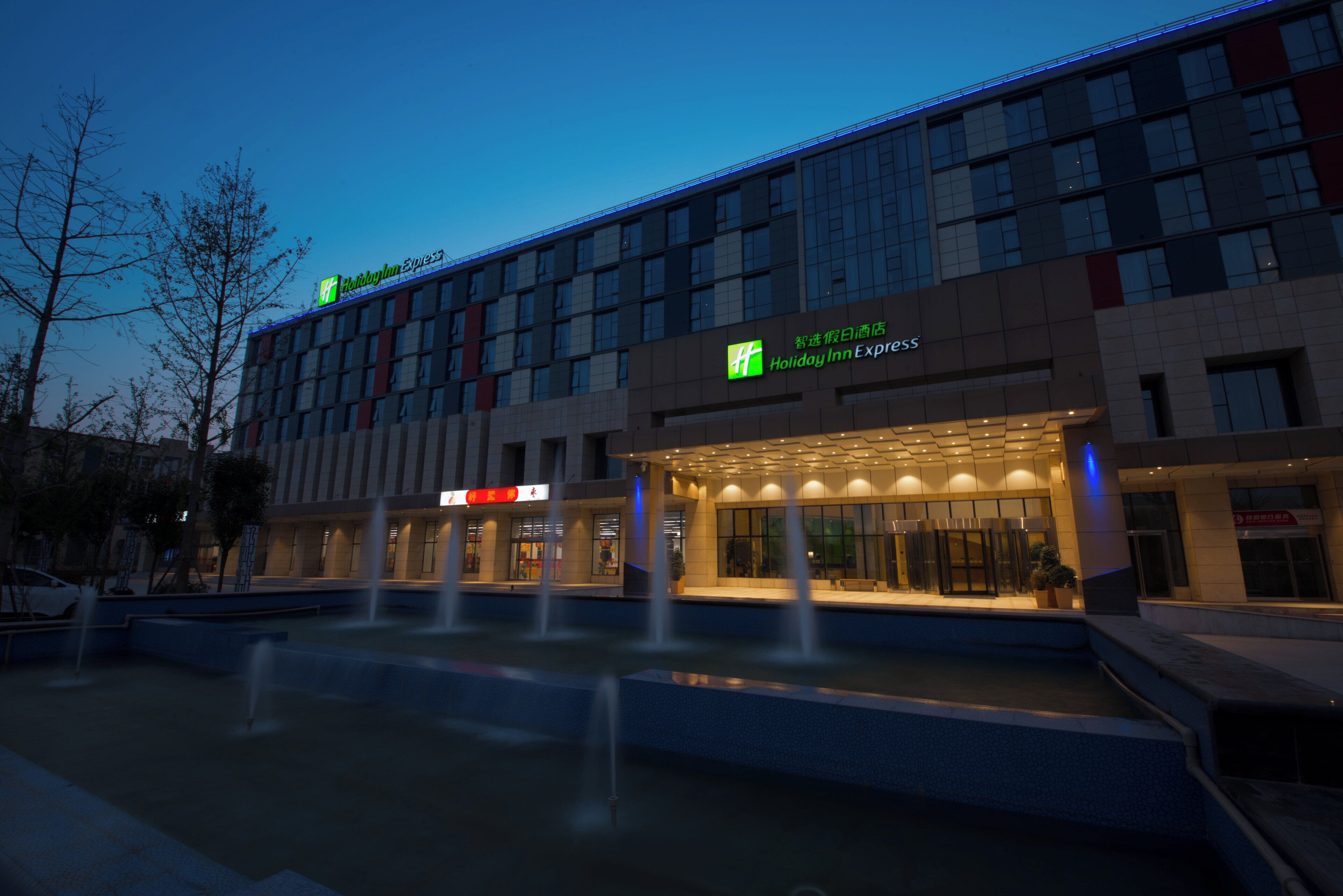 A Holiday Inn Express hotel with a modern facade, a water feature in front, and illuminated signage.