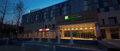 A Holiday Inn Express hotel with a modern facade, a water feature in front, and illuminated signage.